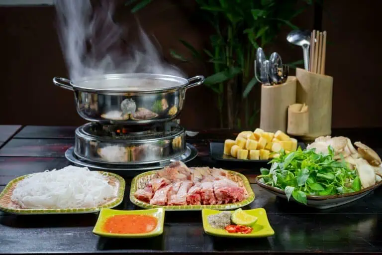 A vibrant table setup of steaming Asian hotpot with fresh noodles, meat, and vegetables.