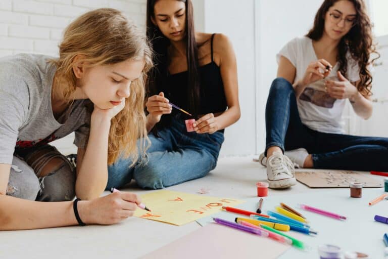 Teenagers collaborating on art projects using paints and pencils, promoting creativity and teamwork.
